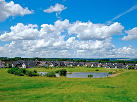 Panoramisch uitzicht over het heuvelachtige landschap van Ferienresort Cochem, met de vakwerkhuizen en een meertje in de Moezelstreek