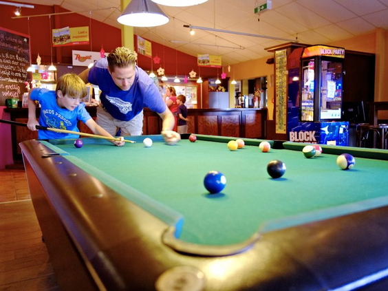 Een vader leert zijn zoon hoe je moet poolen aan de pooltafel in de gezellige bar of indoor speelhal van Ferienresort Cochem.