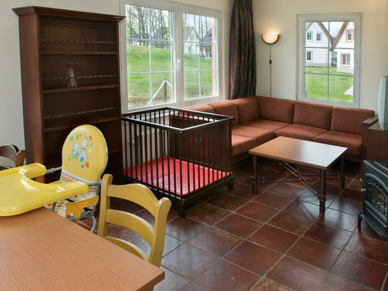 Het kindvriendelijke interieur van een vakantiehuis in Ferienresort Cochem, met een box en kinderstoel in de woonkamer.