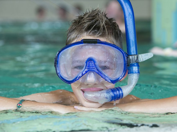Een lachende jongen met een blauwe duikbril en snorkel kijkt in de camera vanuit het binnenzwembad van Ferienresort Cochem.