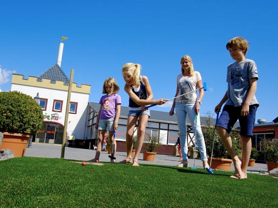 Een groep kinderen speelt op blote voeten een potje midgetgolf op de avontuurlijke midgetgolfbaan van Ferienresort Cochem.