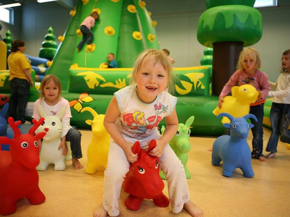 Blije kinderen spelen op hobbelbeesten en ontdekken de kleurrijke speeltoestellen in de indoor speeltuin van Vakantiepark Hasseröder.
