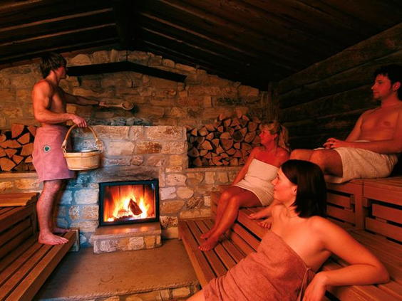 Volwassenen ontspannen in de sfeervolle sauna met stenen muren en een knisperend haardvuur in het wellnesscentrum van Vakantiepark Hasseröder.