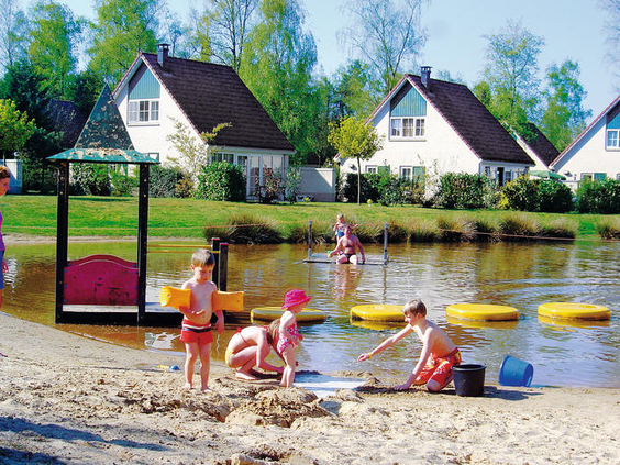 Kinderen bouwen zandkastelen op het strandje aan de recreatieplas van Vakantiepark Hellendoorn.