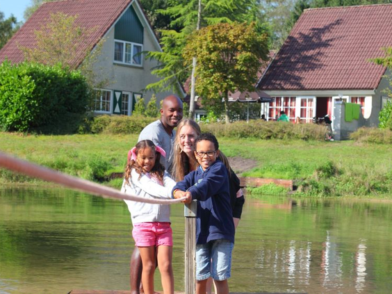 Een lachend gezin maakt gebruik van het trekvlot om de recreatieplas over te steken op Vakantiepark Hellendoorn.