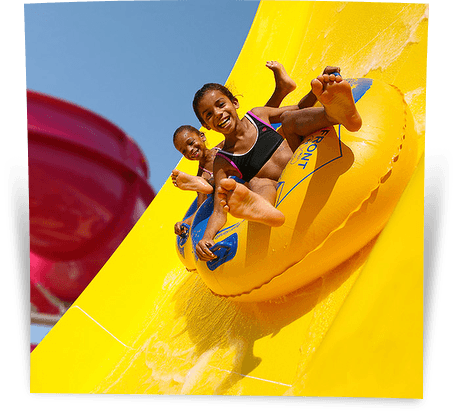 Twee lachende kinderen glijden samen in een opblaasband van een gele waterglijbaan in Aquaventura Slidepark Hellendoorn.