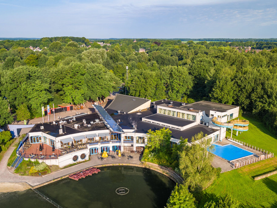 Luchtfoto van Vakantiepark Hunzedal, waarop de centrale gebouwen, de recreatieplas, het zwembad en de groene, bosrijke omgeving in Drenthe te zien zijn.