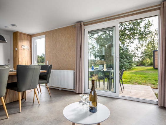 Modern interieur van een vakantiehuisje op Vakantiepark Hunzedal, met uitzicht op de tuin en het terras door de grote schuifpui.