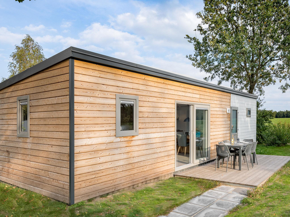 De buitenkant van een modern, houten chalet met een terras en tuin, gelegen in de groene omgeving van Vakantiepark Hunzedal.