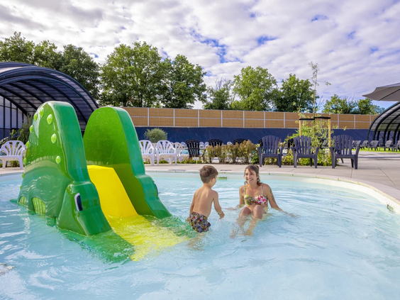 Kinderen spelen bij de kleine groene glijbaan in het ondiepe water