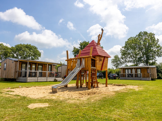 Modern houten chalet met een houten speeltoestel direct voor de deur