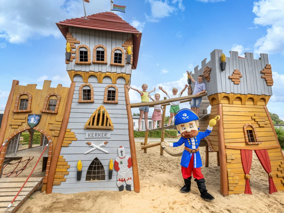 Een groot houten piratenspeelkasteel met een mascotte op de speeltuin van IJsselstrand