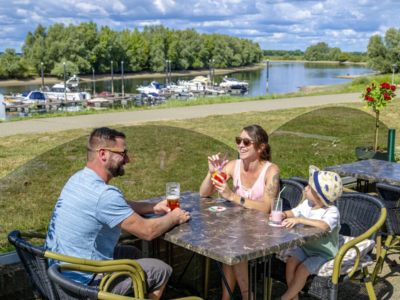 Mensen zitten op het terras van het restaurant met uitzicht op het water en de jachthaven