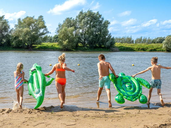 Kinderen spelen met opblaasbare beesten op het zandstrand aan de rivier de IJssel