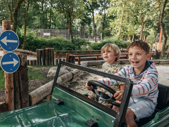 Twee lachende jongens rijden in een groene elektrische auto in het verkeerspark voor kinderen op Vakantiepark Kijkduin.