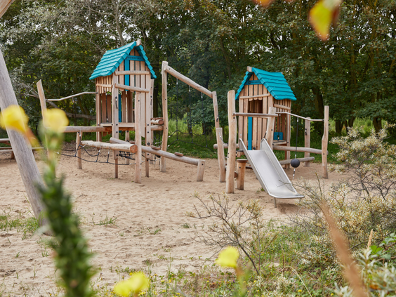 Een avontuurlijke houten speeltuin met een glijbaan en klimtoestellen, gelegen in het zand op Vakantiepark Kijkduin.