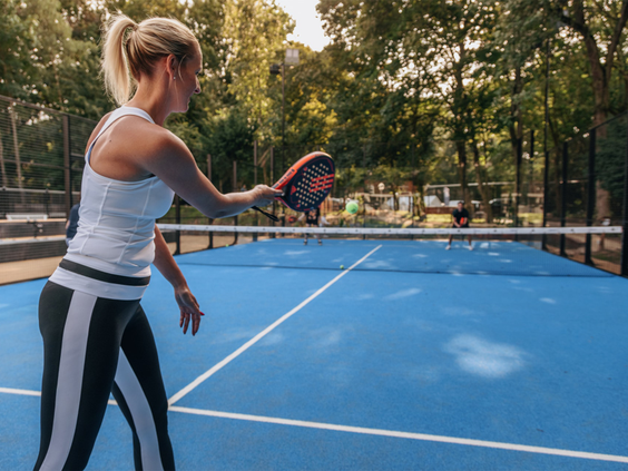 Een vrouw speelt een potje padel op de blauwe, omheinde padelbaan op het sportieve Vakantiepark Kijkduin.
