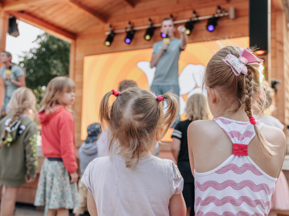 Een groep jonge kinderen kijkt aandachtig naar een show van het animatieteam op het podium bij Vakantiepark Kijkduin.