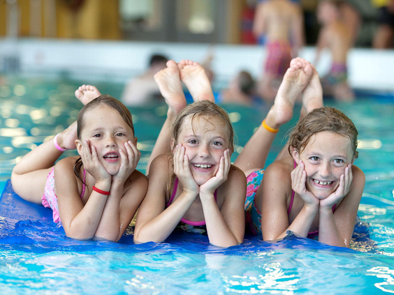 Drie lachende meisjes hebben waterpret op een blauwe mat in het zwembad van Vakantiepark Klein Vink.