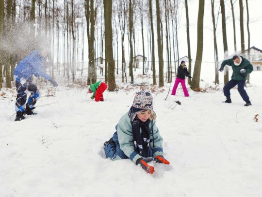 Een familie heeft een groot sneeuwballengevecht in een besneeuwd bos tijdens hun wintervakantie.