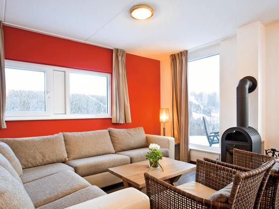 De gezellige woonkamer van een chalet op Landal Winterberg met een comfortabele hoekbank en een knisperende houtkachel.