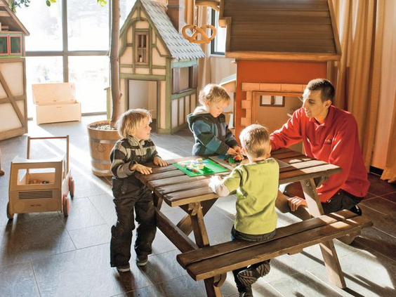Kinderen spelen en knutselen aan een picknicktafel in de gezellige indoorspeelhoek van Landal Winterberg, met houten speelhuisjes op de achtergrond.