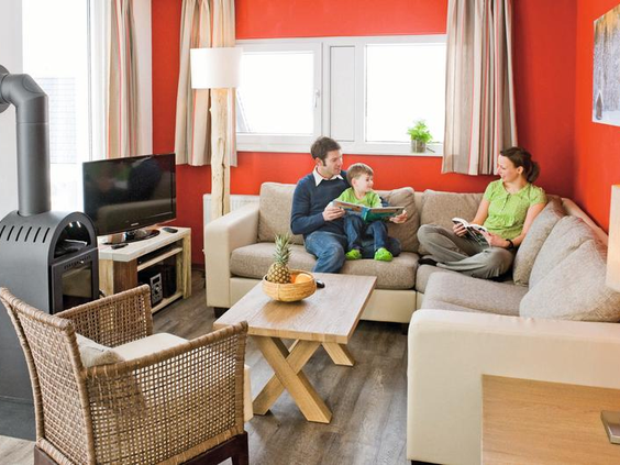 Een gezin met een jong kind ontspant op de bank in de gezellige woonkamer van hun chalet op Landal Winterberg.