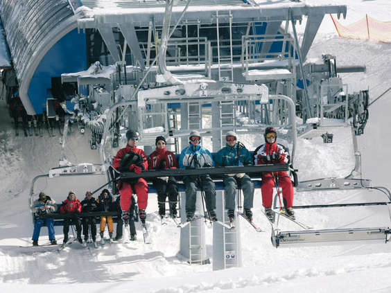 Een groep wintersporters lacht naar de camera terwijl ze in een 6-persoons stoeltjeslift omhoog gaan in het skigebied van Winterberg.