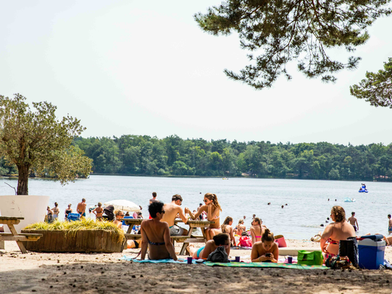 Bezoekers genieten van een zonnige dag op het zandstrand van recreatieplas de IJzeren Man in Vught, vlak bij Vakantiepark Leuvert.