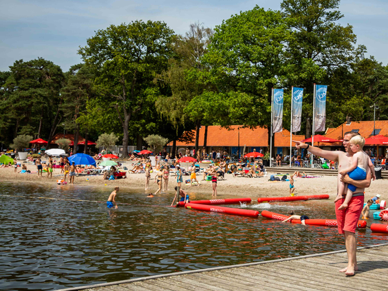 Zonnige dag op het zandstrand van recreatieplas de IJzeren Man in Vught, waar gezinnen zwemmen en zonnen, dicht bij Vakantiepark Leuvert.
