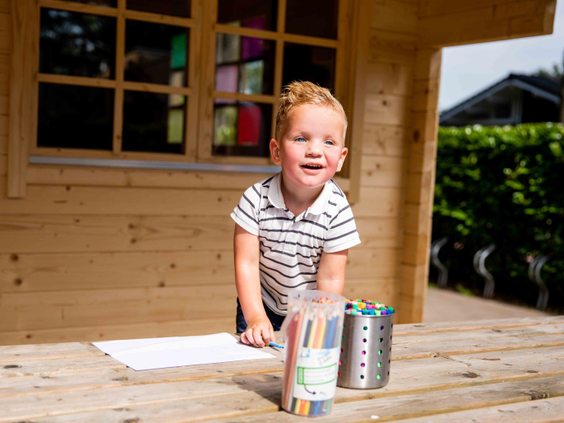 Een jonge jongen staat enthousiast te kleuren en knutselen aan een houten tafel bij de Kidsclub van Vakantiepark Leuvert.