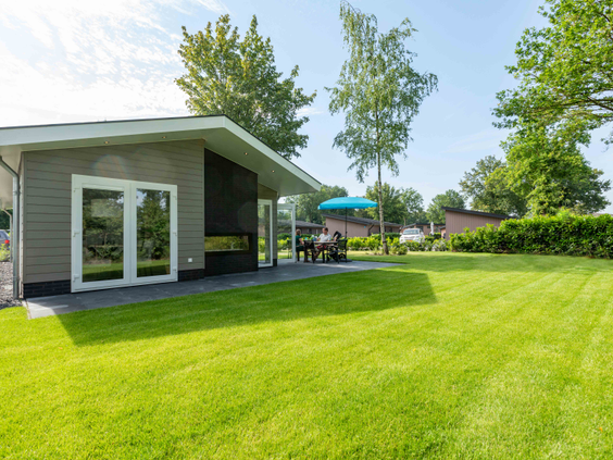Een modern chalet met een groot, zonnig grasveld ervoor, waar kinderen alle ruimte hebben om te spelen op Vakantiepark Leuvert.