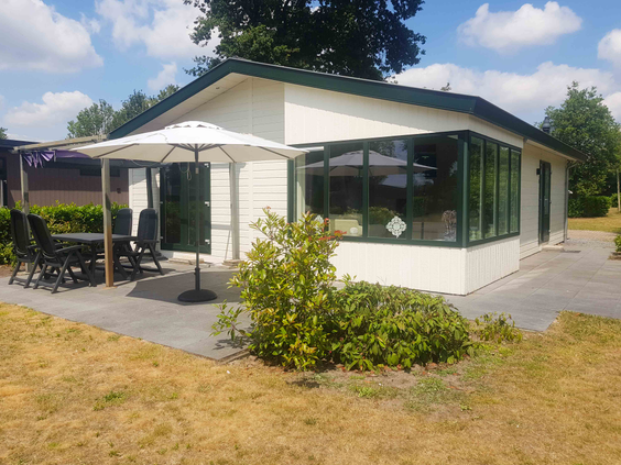 Een vrijstaand, wit chalet met een ruim terras en tuinmeubilair, gelegen in het groen van Vakantiepark Leuvert.