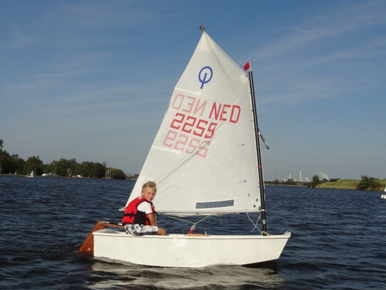 Een jongen krijgt zeilles en vaart in een Optimist zeilboot op het water bij Vakantiepark Marina Beach in Zeeland.