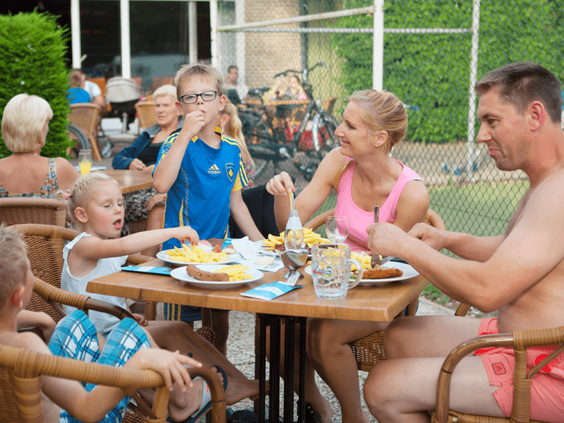 Een gezin met kinderen eet gezellig frietjes en snacks op het terras van het restaurant op Vakantiepark Marina Beach.