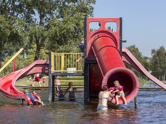 Kinderen glijden van een grote rode waterglijbaan die uitkomt in de recreatieplas bij Vakantiepark Marina Beach.