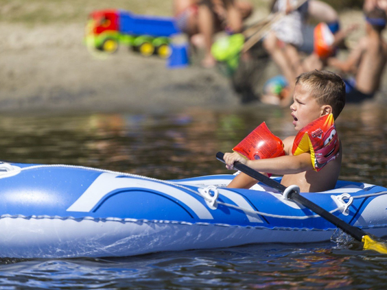 Een jongen met zwemvest peddelt in een opblaasbare boot op de recreatieplas van Vakantiepark Marina Beach.