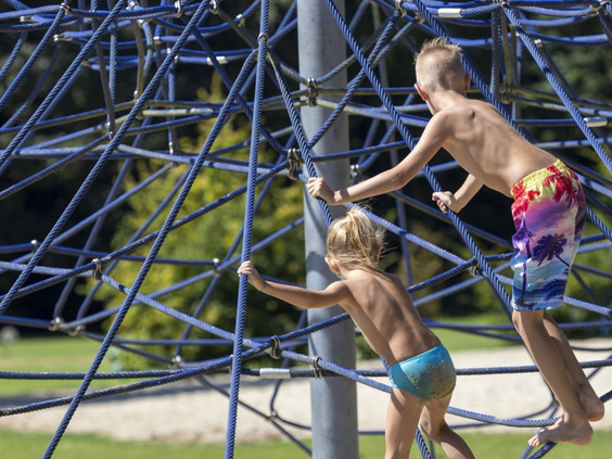 Kinderen klimmen en klauteren op een groot blauw web-klimrek in de buitenspeeltuin van Vakantiepark Marina Beach.