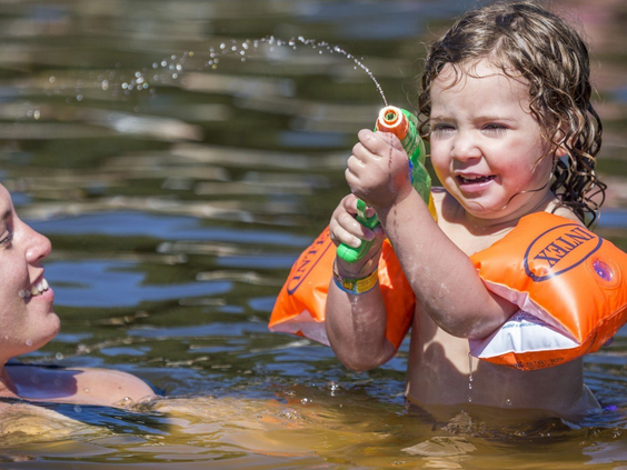 Een klein kind met zwembandjes heeft plezier met een waterpistool in de recreatieplas van Vakantiepark Marina Beach.