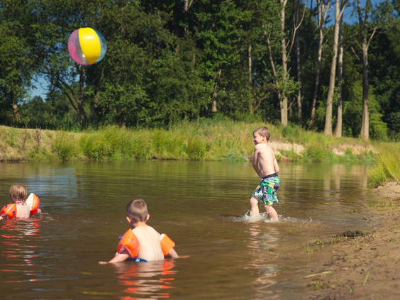 Twee jongens spelen met een bal in het ondiepe water van de rivier de Regge bij Vakantiepark Molke op een zonnige dag.
