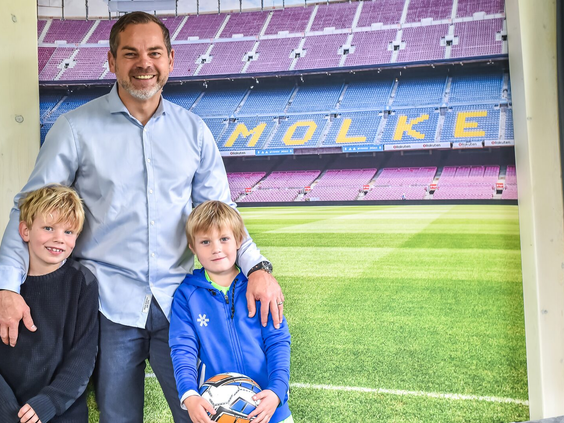 Een vader en zoon poseren voor de muur van een voetbalstadion-tribune in de speciale voetbal-lodge van Vakantiepark Molke.