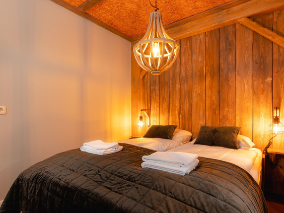 Een sfeervolle slaapkamer met opgemaakte bedden en een houten wand in een accommodatie op Vakantiepark Molke.