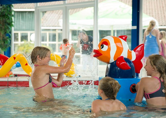 Kinderen spelen in het peuterbad van het binnenzwembad op Vakantiepark Molke, met een spuitend vis-speeltoestel.