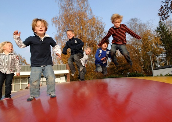 Een groep blije kinderen springt hoog in de lucht op de grote rode luchttrampoline van Vakantiepark Molke.