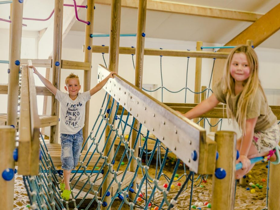 Kinderen klimmen over een touwbrug in de houten binnenspeeltuin van Vakantiepark Molke.