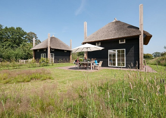 Twee luxe, zwarte Regge Lodges met rieten dak en een terras met een familie aan een tuintafel op Vakantiepark Molke.