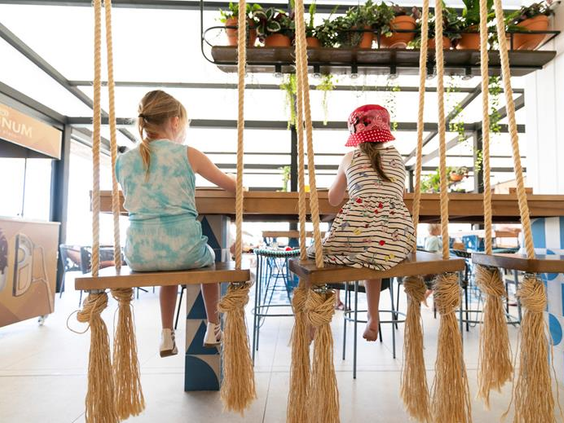 Twee kinderen zitten op unieke schommelstoelen aan een tafel in het familierestaurant van Parque Cristobal.