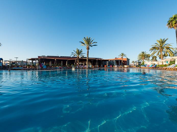 Het grote, helderblauwe zwembad van vakantiepark Parque Cristobal, omringd door palmbomen onder een strakblauwe hemel.
