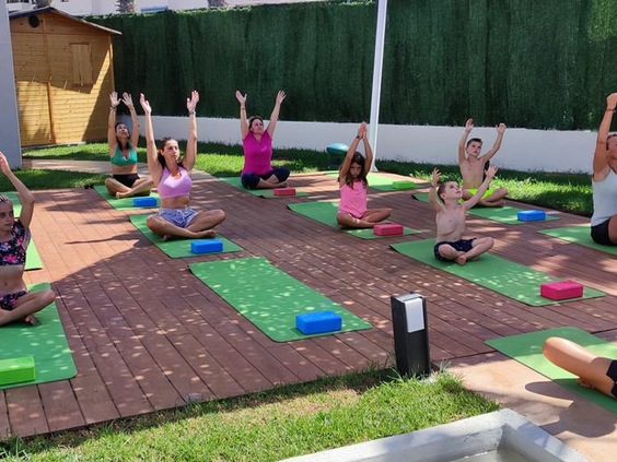 Kinderen doen mee aan een leuke outdoor yoga-les op gekleurde matjes in de tuin van Parque Cristobal.