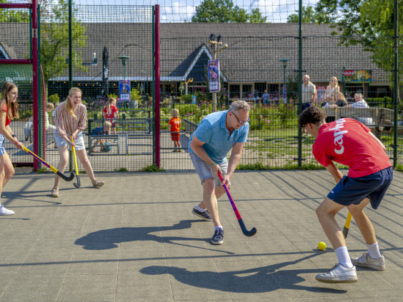 Kinderen en volwassenen spelen hockey op het multisportveld van de camping